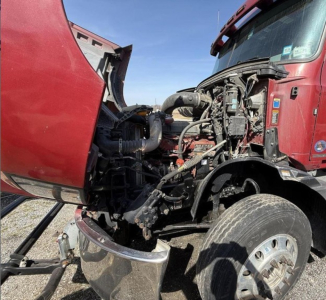 Truck engine bay visible with damaged front; red Mack Anthem cab with exposed engine, hoses, and components.