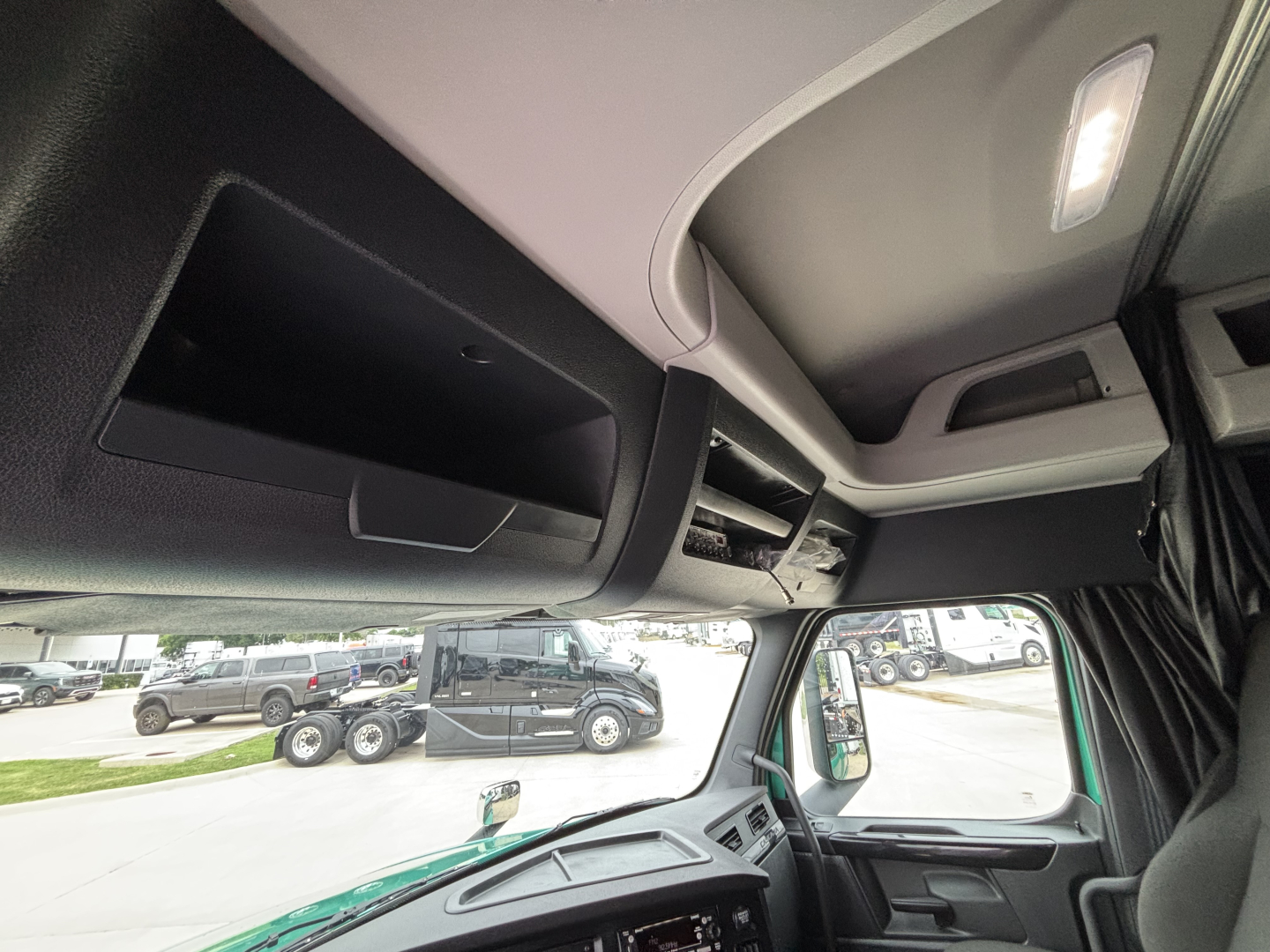 Cab interior of a Freightliner Cascadia 126 truck showing overhead storage compartments and skylight; dashboard and windshield with exterior lot in background.