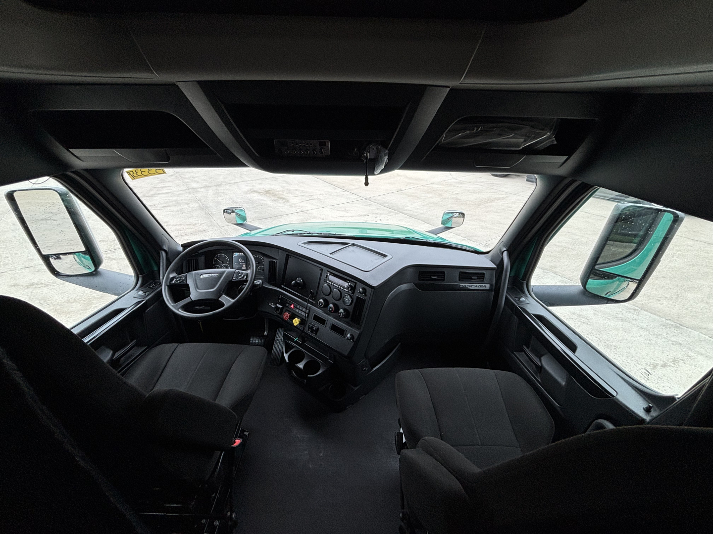 Freightliner Cascadia 126 cab interior showing steering wheel, dashboard, and twin front seats.