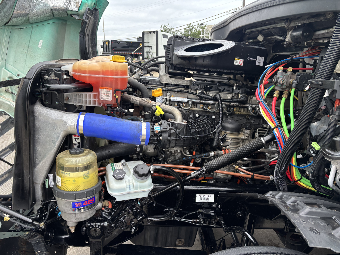 Freightliner Cascadia 126 engine bay showing coolant reservoir, air intake, braided hoses, wiring harness, and various fluid reservoirs.