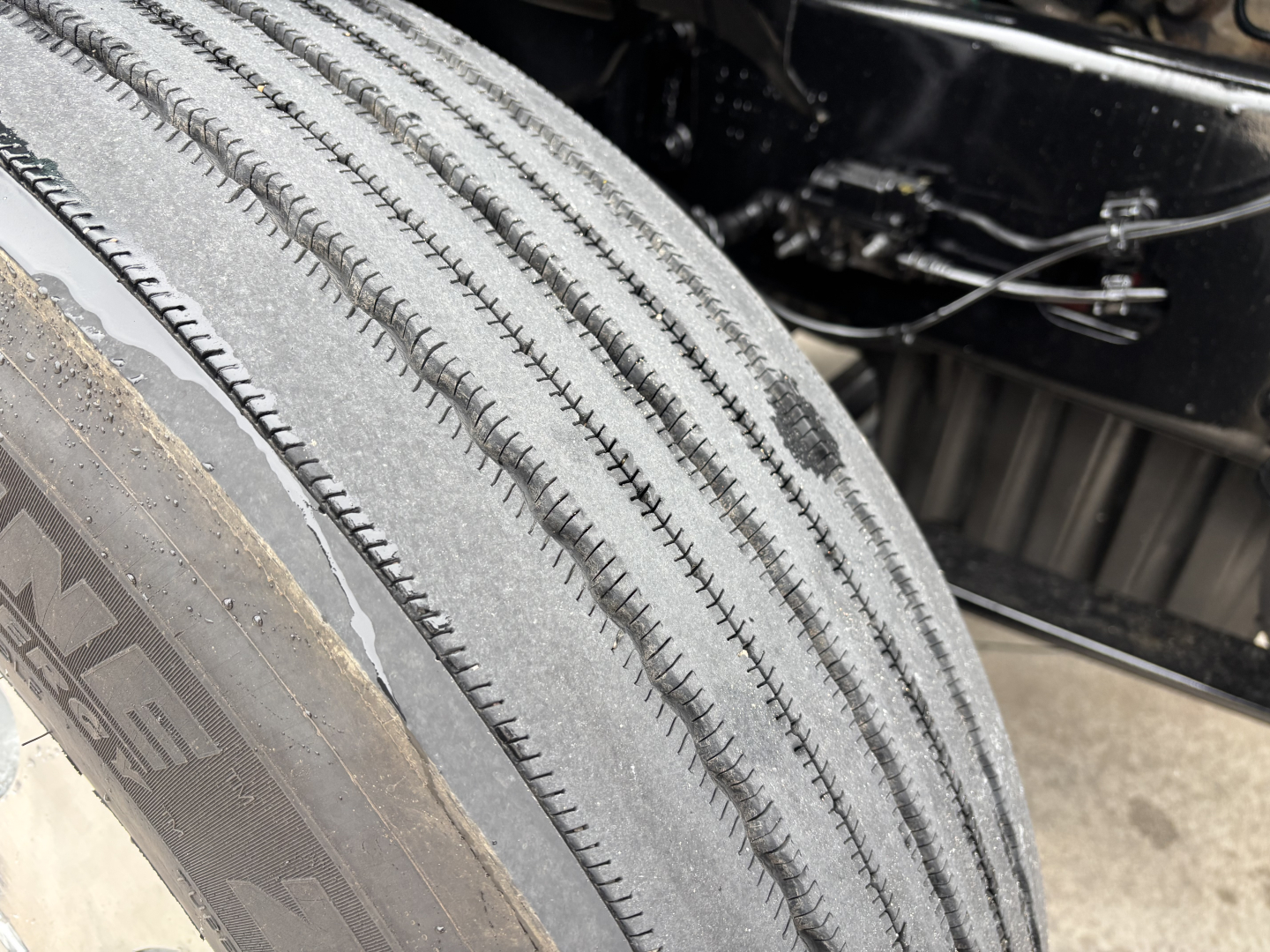 Truck tire close-up view with tread pattern on a Freightliner Cascadia 126 front wheel assembly showing worn tread lines.