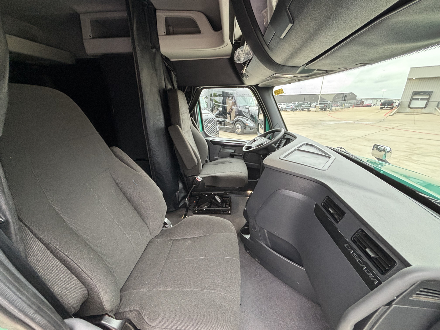 Cab interior of a 2023 Freightliner Cascadia 126 showing driver seat, passenger seat, dashboard, and steering wheel.