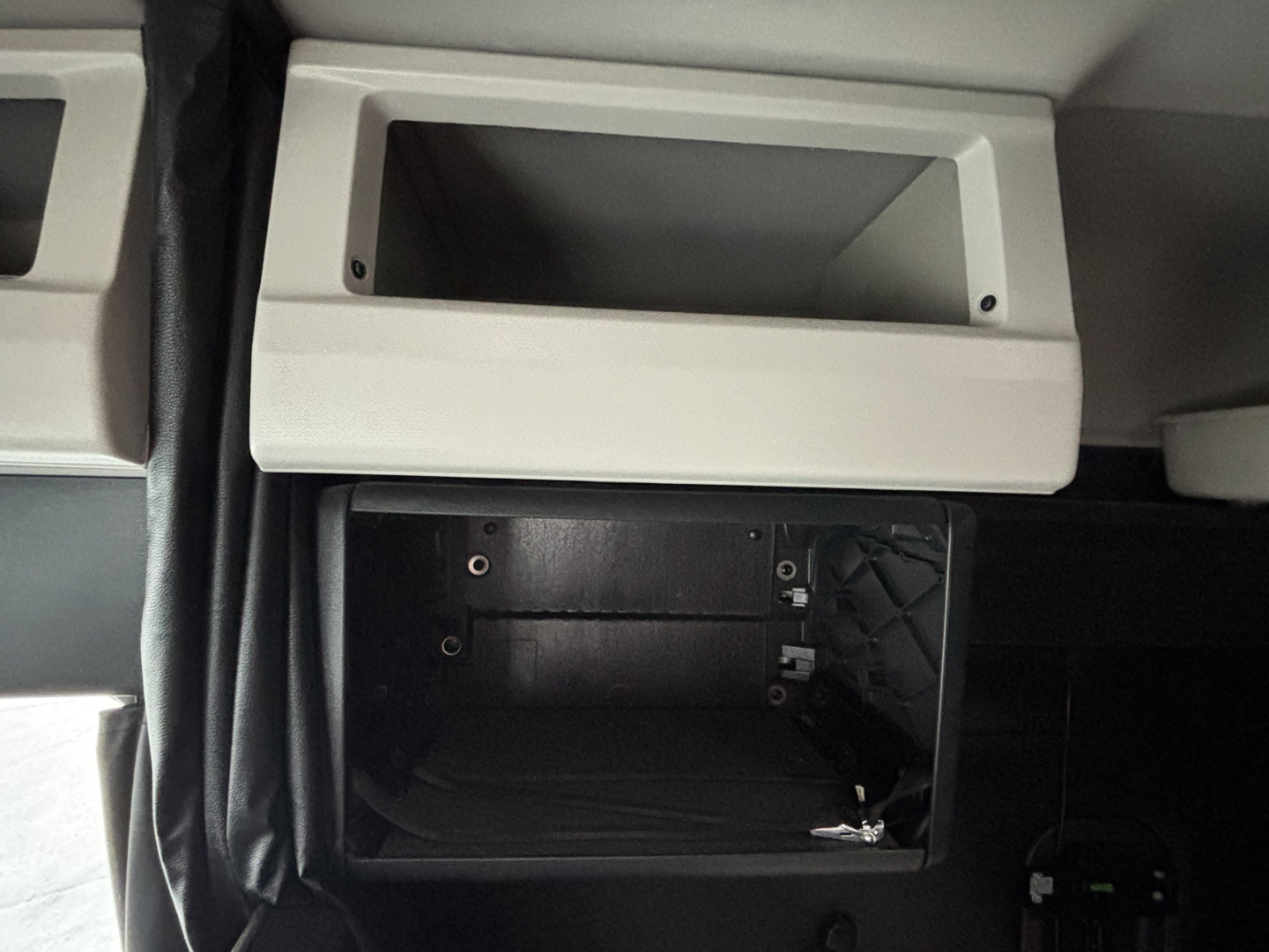 Cab interior of a Freightliner Cascadia 126 showing an empty overhead storage cubby and a recessed glove/diag panel with visible screws.
