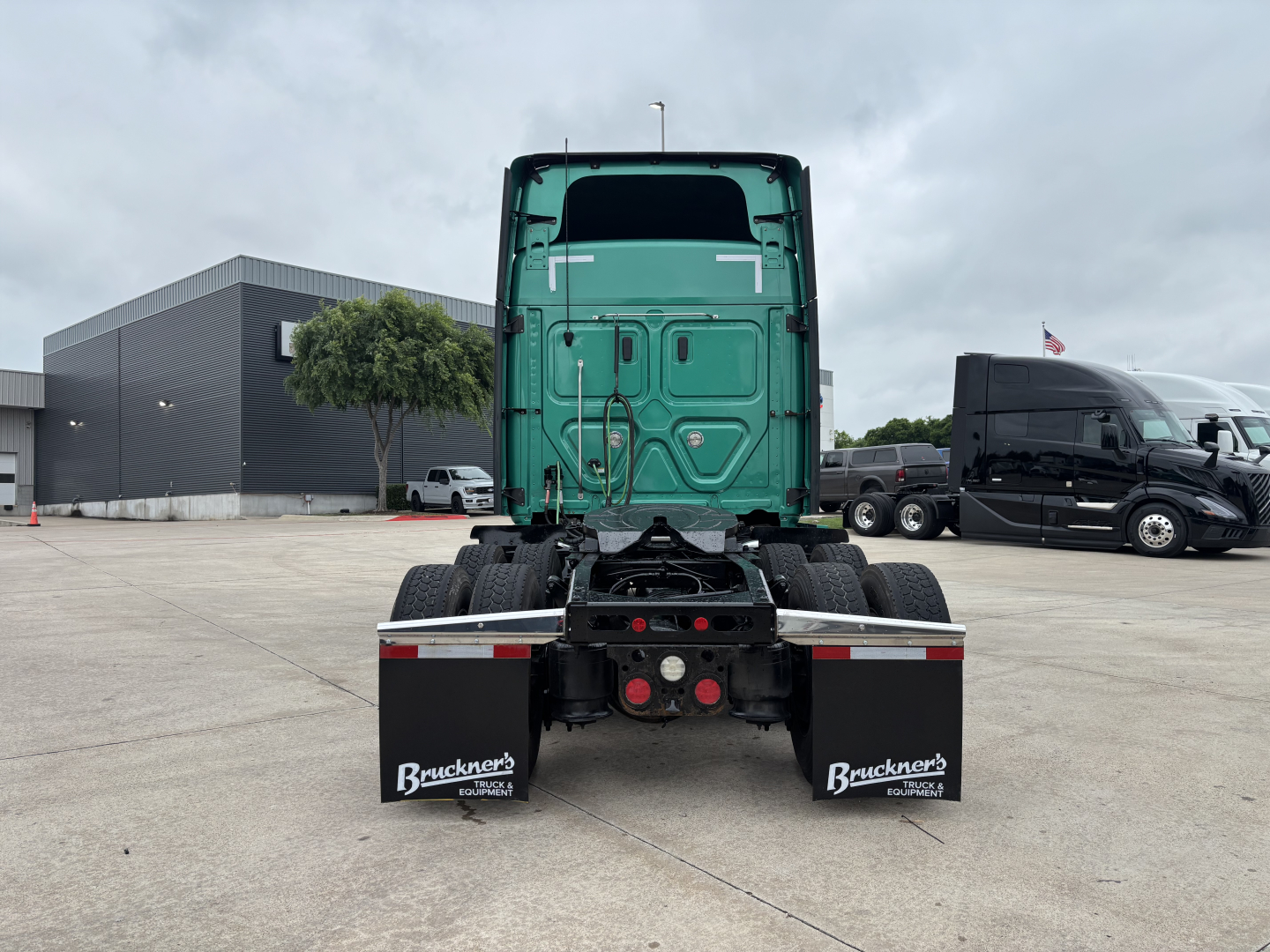 Truck chassis rear view with green cab and dual mud flaps showing Bruchner's logo at trailer connection area.