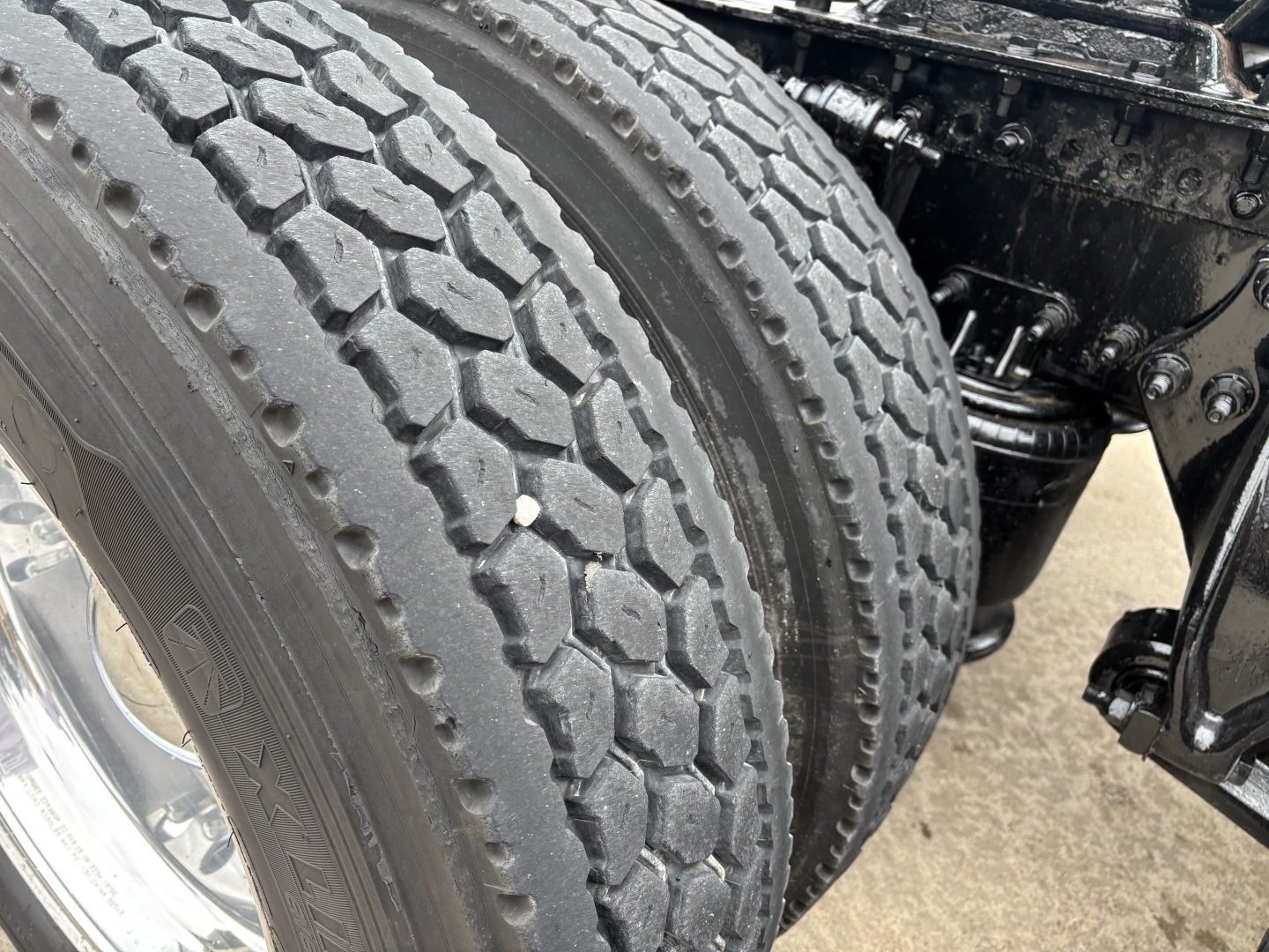 Tire tread close-up on Freightliner Cascadia 126 truck showing dual rear axle components and suspension links.