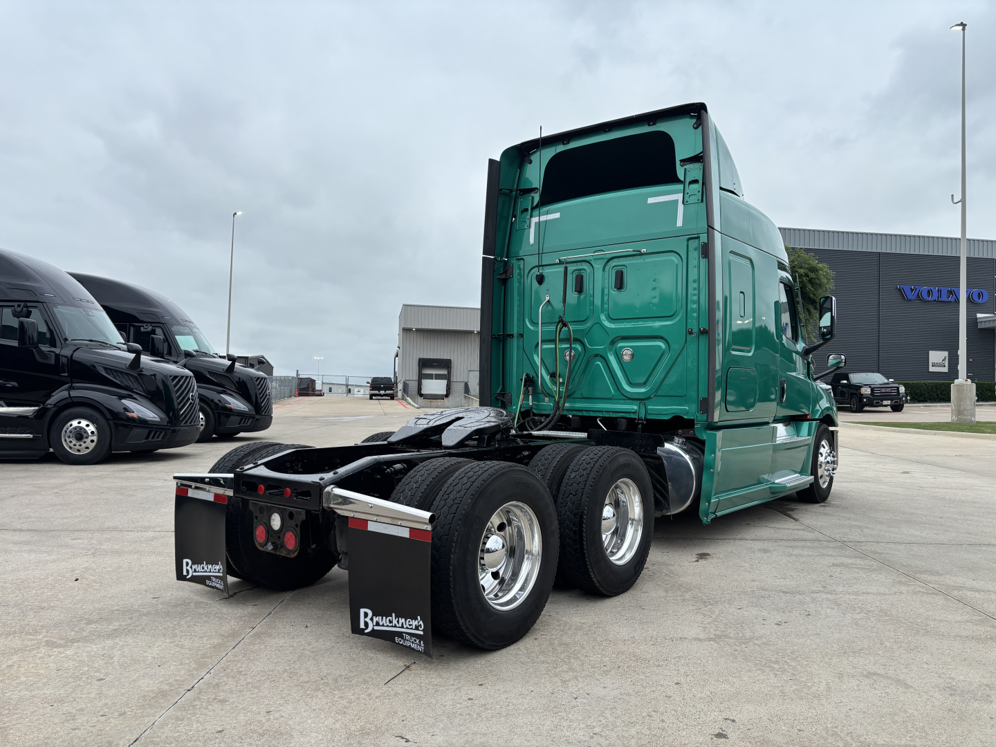 Freightliner Cascadia 126 tractor rear/side view showing dual rear axles and fifth-wheel area, green sleeper cab, dealership lot in background.