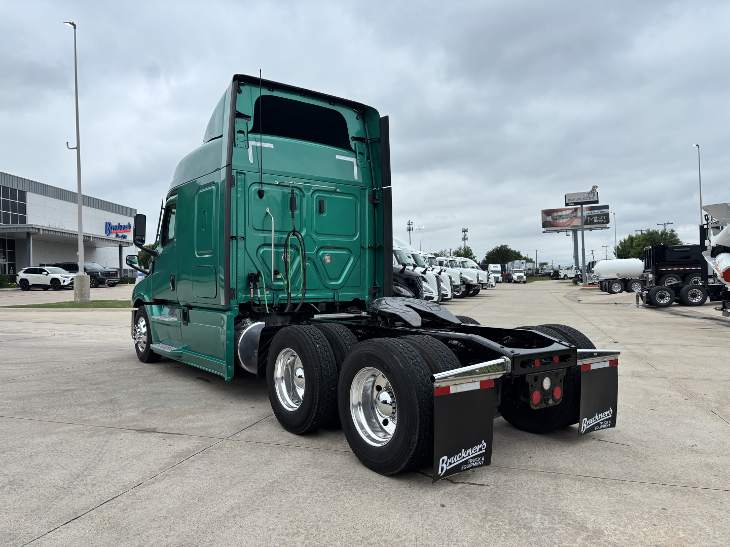 Truck cab and rear view showing green 2023 Freightliner Cascadia 126, semi-truck chassis, dual rear axles, mudflaps, and fifth-wheel area in a dealership lot.