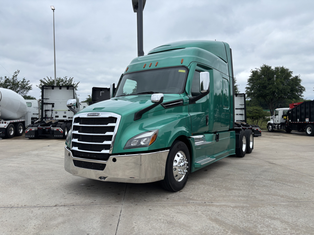 Freightliner Cascadia 126 semi-truck tractor in green with chrome bumper, sleeper cab, set in a truck lot.