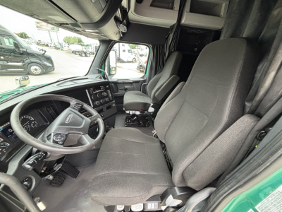 Truck cab interior of a Freightliner Cascadia 126 showing steering wheel, driver seat, passenger seat, dashboard with gauges and controls, and overhead compartments.