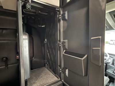 Truck cab interior storage compartment open door showing shelves and molded pockets; Freightliner Cascadia 126 dash area visible outside.