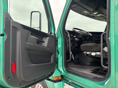 Cab interior of a green Freightliner Cascadia 126 with front door open, showing steering wheel, dashboard, and driver's seat in view.