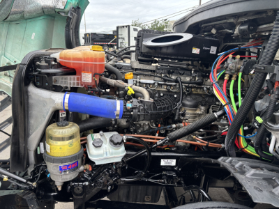 Freightliner Cascadia 126 engine bay showing coolant reservoir, air intake, braided hoses, wiring harness, and various fluid reservoirs.