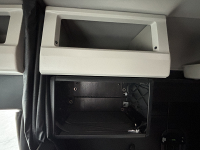 Cab interior of a Freightliner Cascadia 126 showing an empty overhead storage cubby and a recessed glove/diag panel with visible screws.