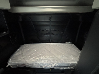 Truck sleeper cab interior with plastic-covered mattress and storage net beyond. Freightliner branding visible on back wall.
