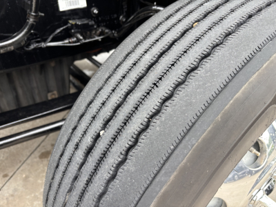 Truck wheel and tire of a Freightliner Cascadia 126 showing tread and sidewall with surrounding chassis components.