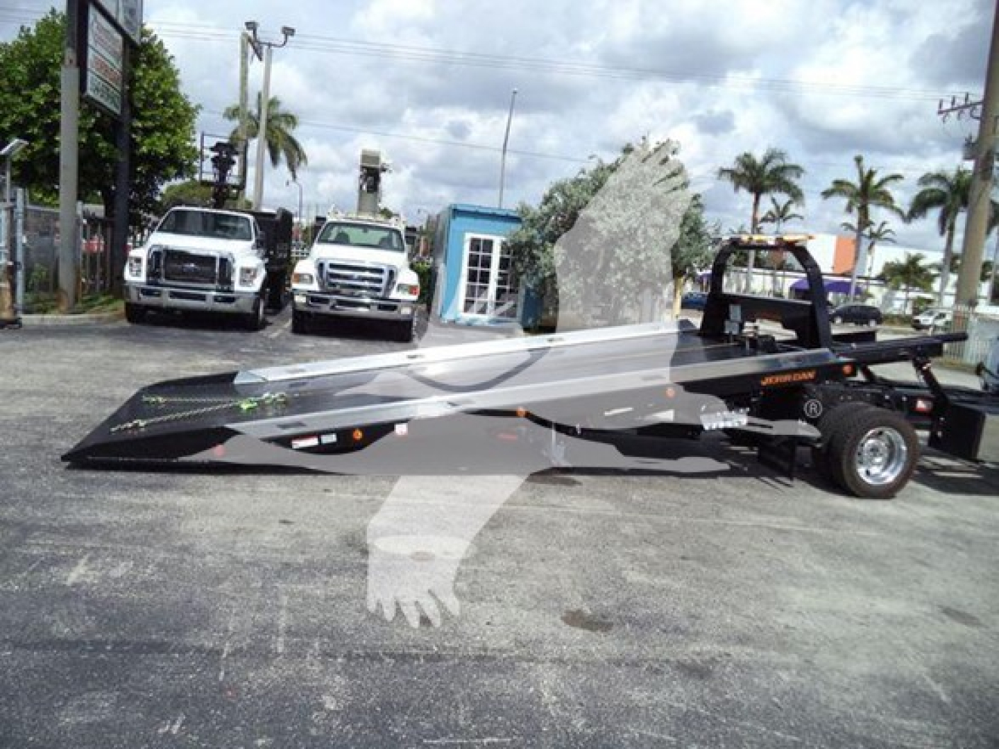 2024 Ford F550 roll-back tow truck with a flatbed in a dealership lot, units in background.