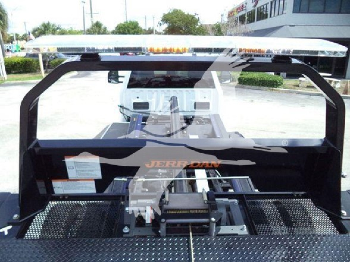 Ford F550 rollback truck bed with Jerr-Dan tow equipment and metal diamond-plate platform, pickup style rear with light bar on top and hydraulic winch assembly visible.