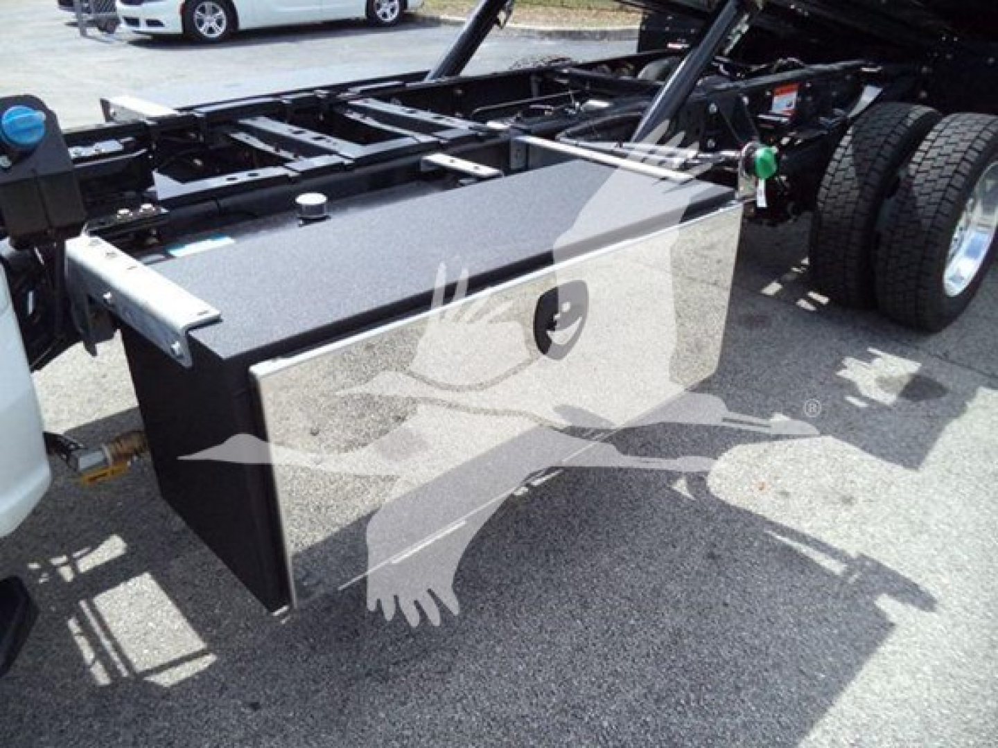 Ford F-550 rollback chassis showing metal tool/maintenance box mounted under frame with fuel tank cap visible, part of truck bed and dual rear wheels.