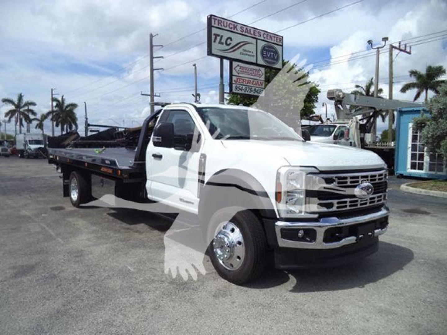Ford F-550 rollback tow truck in a dealership lot with white cab and long flatbed.