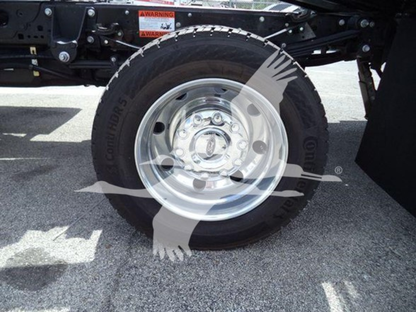 Ford F-550 rollback truck wheel and front suspension with alloy wheel and tire, partial undercarriage, warning sticker visible