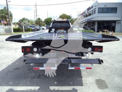 Ford F-550 rollback flatbed tow truck rear view showing loading flaps, taillights, and metal step plates.