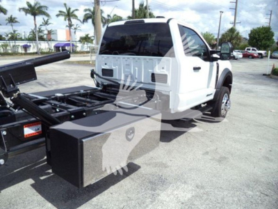 Ford F-550 rollback tow truck with white cab and black heavy-duty toolbox on side, external hitch and hydraulic bed components visible.