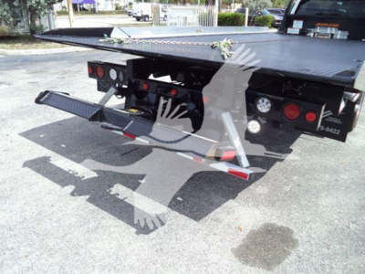 Ford F-550 rollback truck rear with hydraulic tow bed and safety lighting visible.