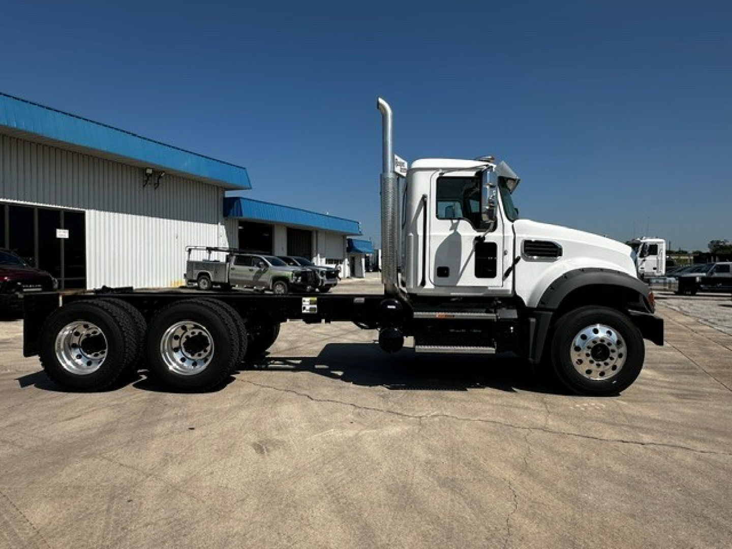 Mack GR64F cab and chassis truck side view showing white cab, dual rear axles, and silver exhaust stack.
