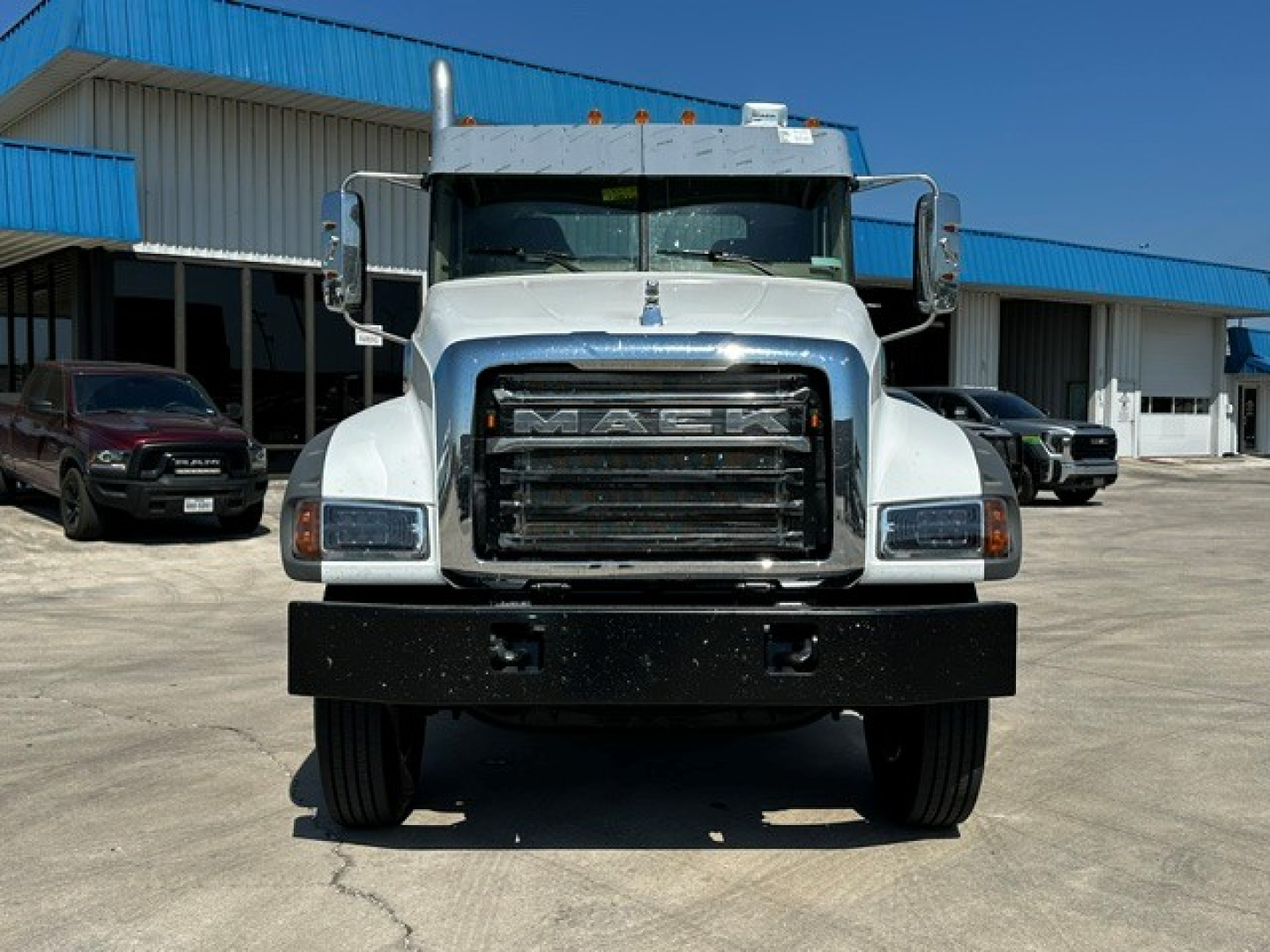 Front view of a white 2027 Mack GR64F cab and chassis showing large black grille with MACC logo, rectangular headlights, and a heavy front bumper.