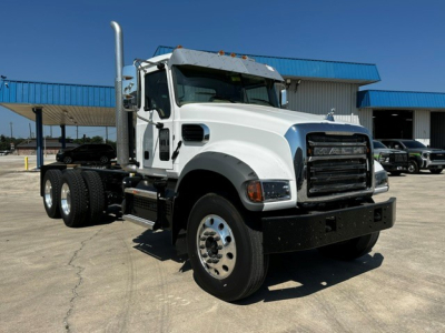 Mack GR64F cab and chassis truck in white, front three-quarter view, with chrome exhaust stack, black bumper, large front grille, and dual rear axles.