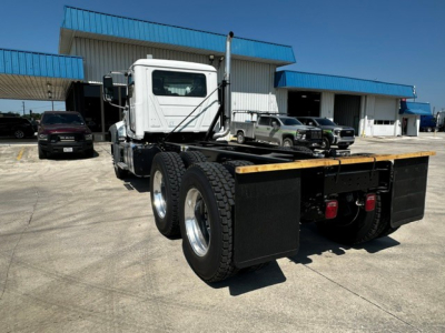 Flatbed truck chassis showing rear view with dual rear axles and flat wooden deck, white cab, in-service industrial lot.