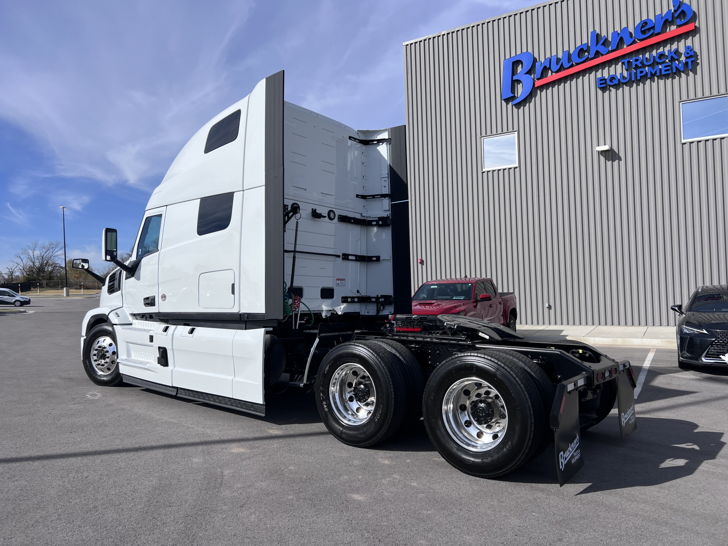 Semi truck tractor in a parking lot showing white cab and dual rear axles with chrome wheels near a building labeled Buckner’s Truck Equipment.