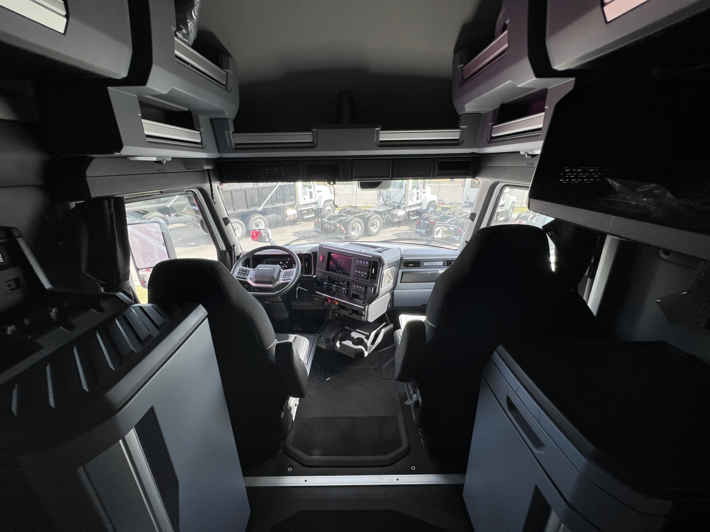 Cab interior view of a 2026 Mack PR64T76H truck showing dashboard, steering wheel, captain seats, overhead compartments, and driver area