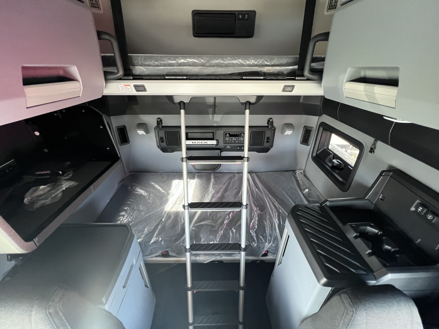 Mack PR64T76H conventional sleeper cabin interior showing ladder, dashboard panels, overhead storage, and window; multiple compartments and controls visible.