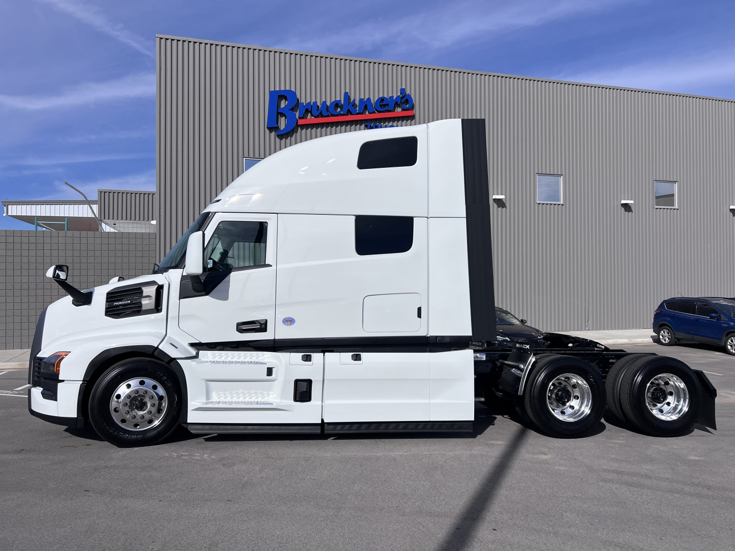 Semi truck tractor in white with raised sleeper cab side view showing Mack PR64T76H spec details on the cab and chassis.