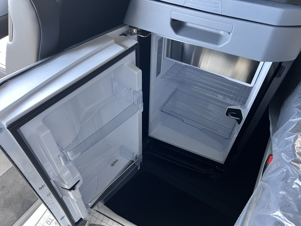 Truck refrigerator compartment in a new Mack PR64T76H cab showing open lower and upper freezers with shelves.