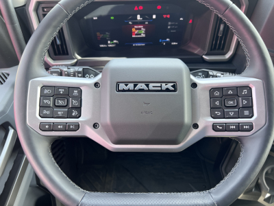 Mack PR64T76H steering wheel center with Mack logo and dashboard behind, control buttons on both left and right spokes visible.