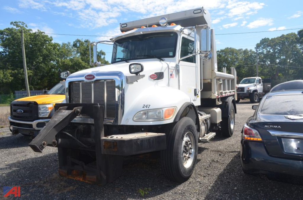 Peterbilt 348 dump truck side front view showing front bumper and large plow attachment with chrome grille and white cab.