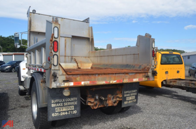 Peterbilt 348 dump truck rear view showing rusted dumping bed and taillights, with contact plaques on mud flaps and a yellow truck in background