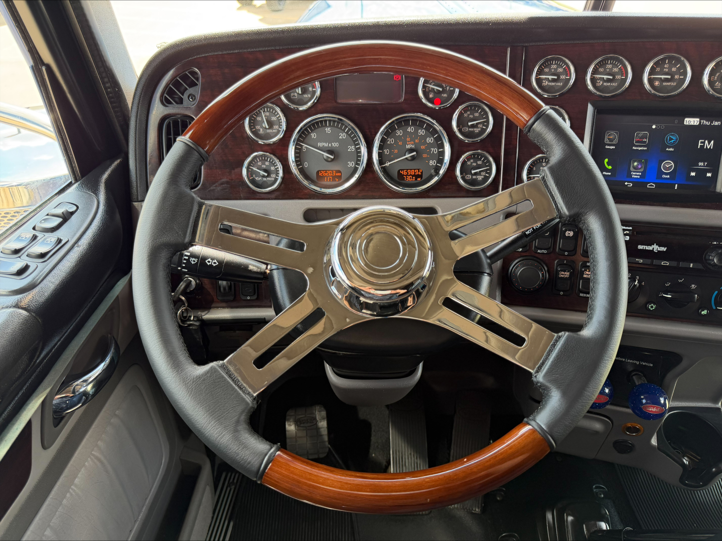 Steering wheel and dashboard of a 2022 Peterbilt 389 conventional sleeper truck showing multiple analog gauges and a digital display.