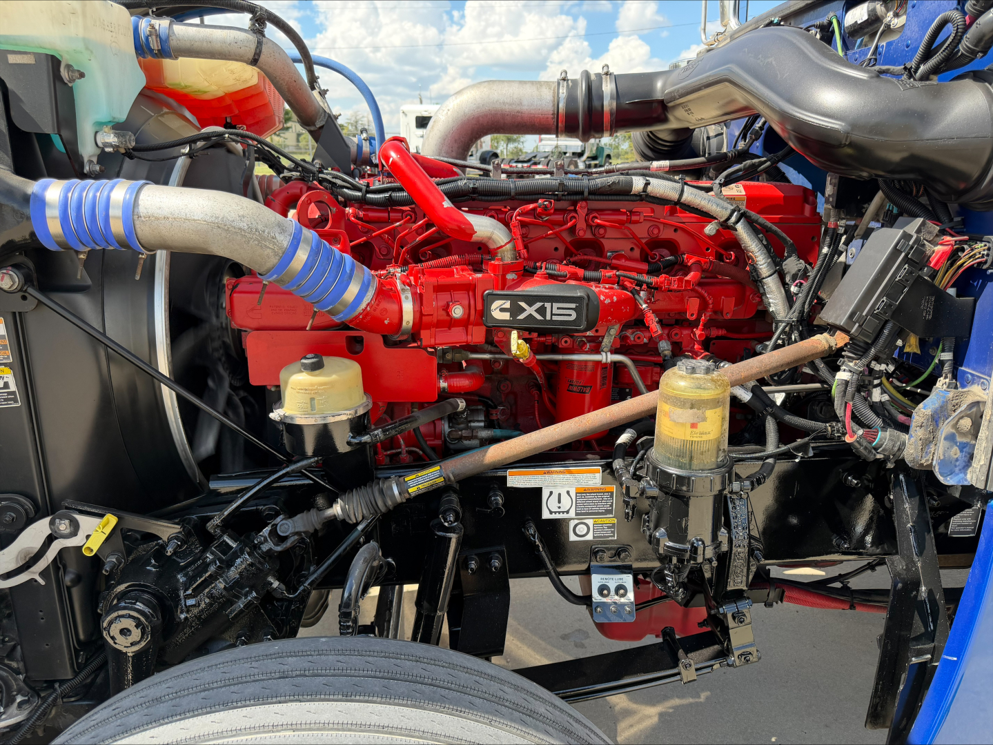 Peterbilt 389 engine bay showing red diesel engine with X15 badge, various hoses, reservoirs, and components.