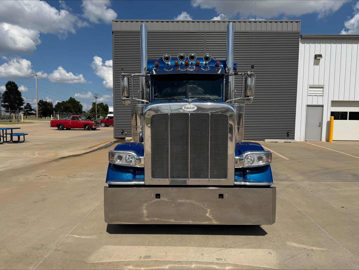 Peterbilt 389 front view showing chrome grille, large bumper, two air intakes, and blue cab with multiple lights on the roof.