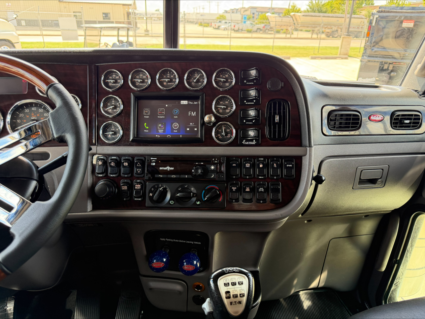 Peterbilt 389 truck interior dashboard with numerous gauges, center touchscreen, gear shifter, and control switches.