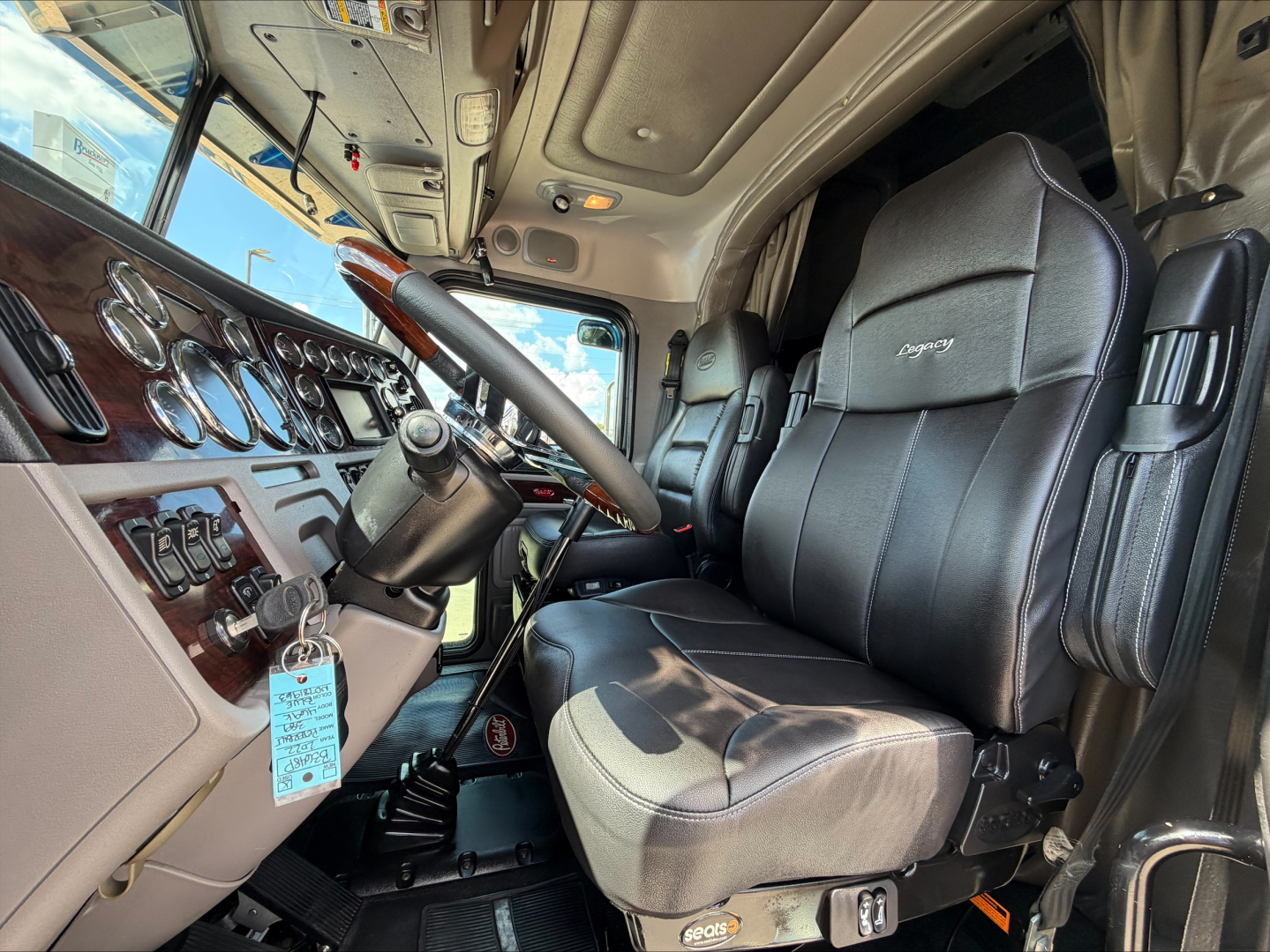 Interior of a 2022 Peterbilt 389 cab showing steering wheel, dashboard with gauges, and driver seat with tag hanging from ignition