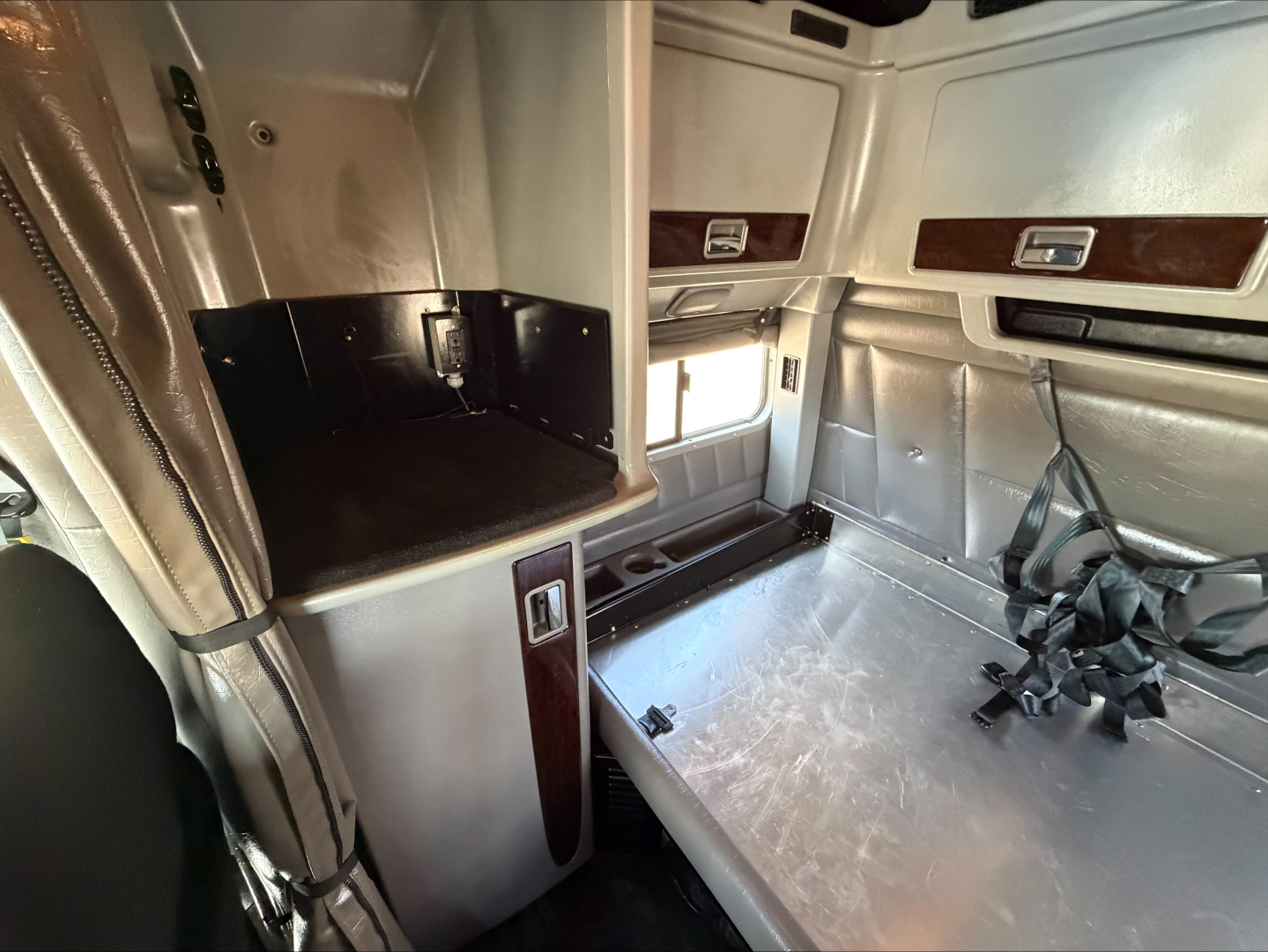 Peterbilt 389 sleeper cab interior showing storage compartments and sleeping/bench area with metal surface and seat belts.
