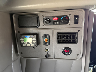 Peterbilt 389 dash panel showing controls and gauges, HVAC knobs, digital display, circular gauge, and vent panel.