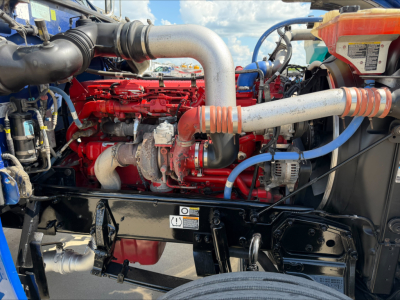 Peterbilt 389 engine bay showing large aluminum intake pipe, red engine block with hoses and electrical wiring, and blue coolant lines.
