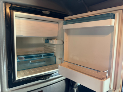 Peterbilt 389 truck sleeper cab area showing an open compact fridge with shelves and a small freezer compartment inside.