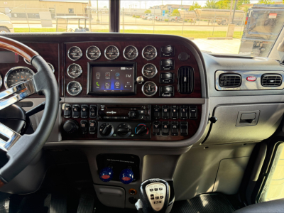 Peterbilt 389 truck interior dashboard with numerous gauges, center touchscreen, gear shifter, and control switches.