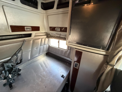 Peterbilt truck sleeper cab interior showing bed area with seat belts and overhead compartments; metallic silver with wood trim panels.
